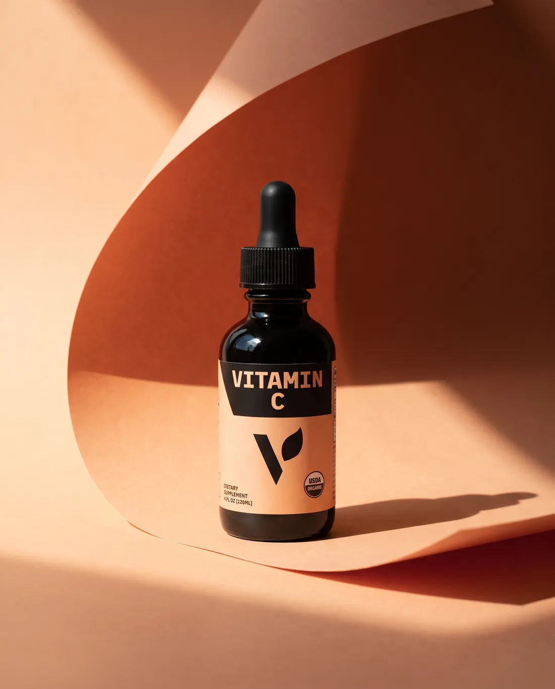 Organic Vitamin C dropper bottle in a curl of peach paper, in hard sunlight