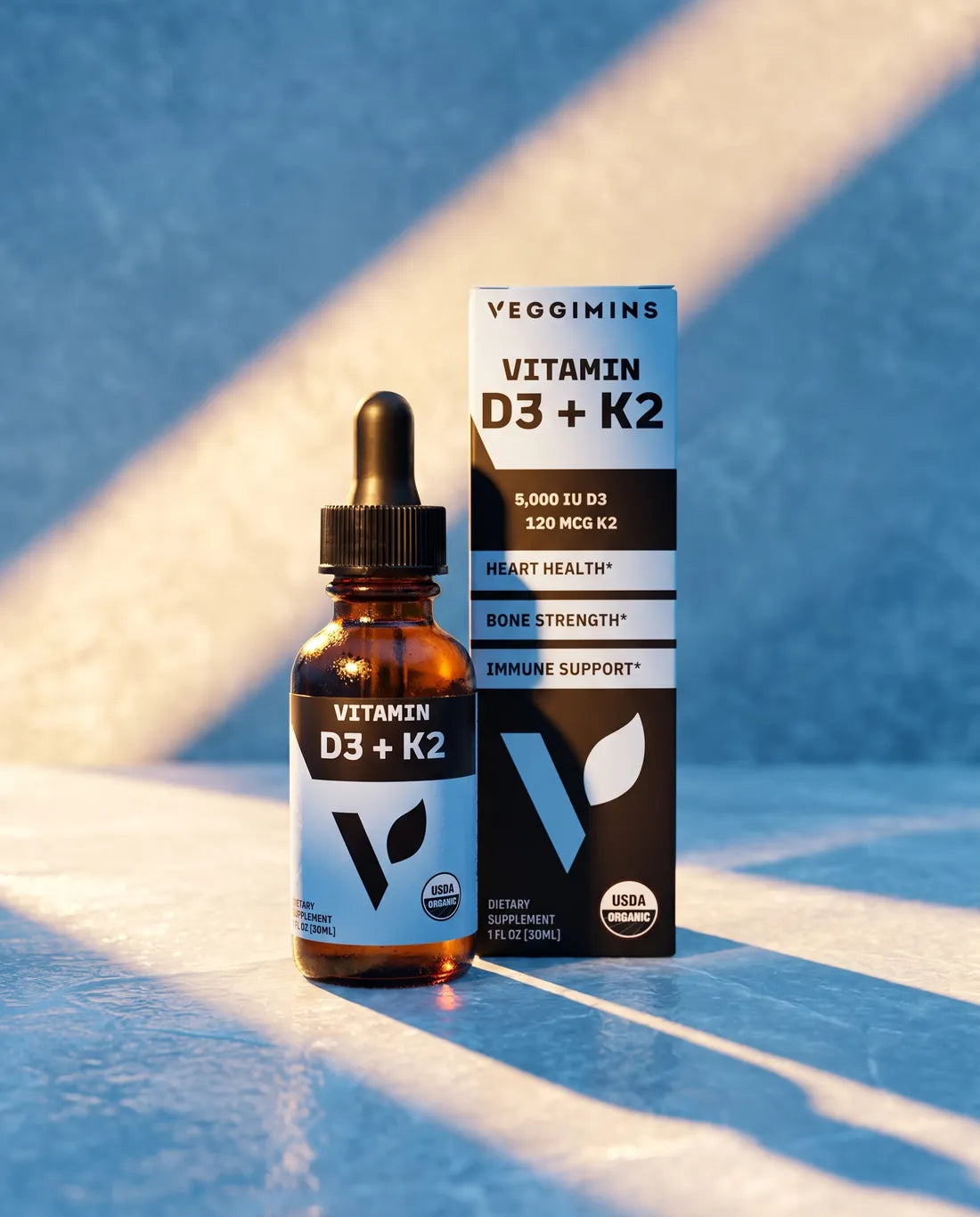 Vitamin D3 + K2 dropper bottle and box in a beam of sunlight on a blue surface